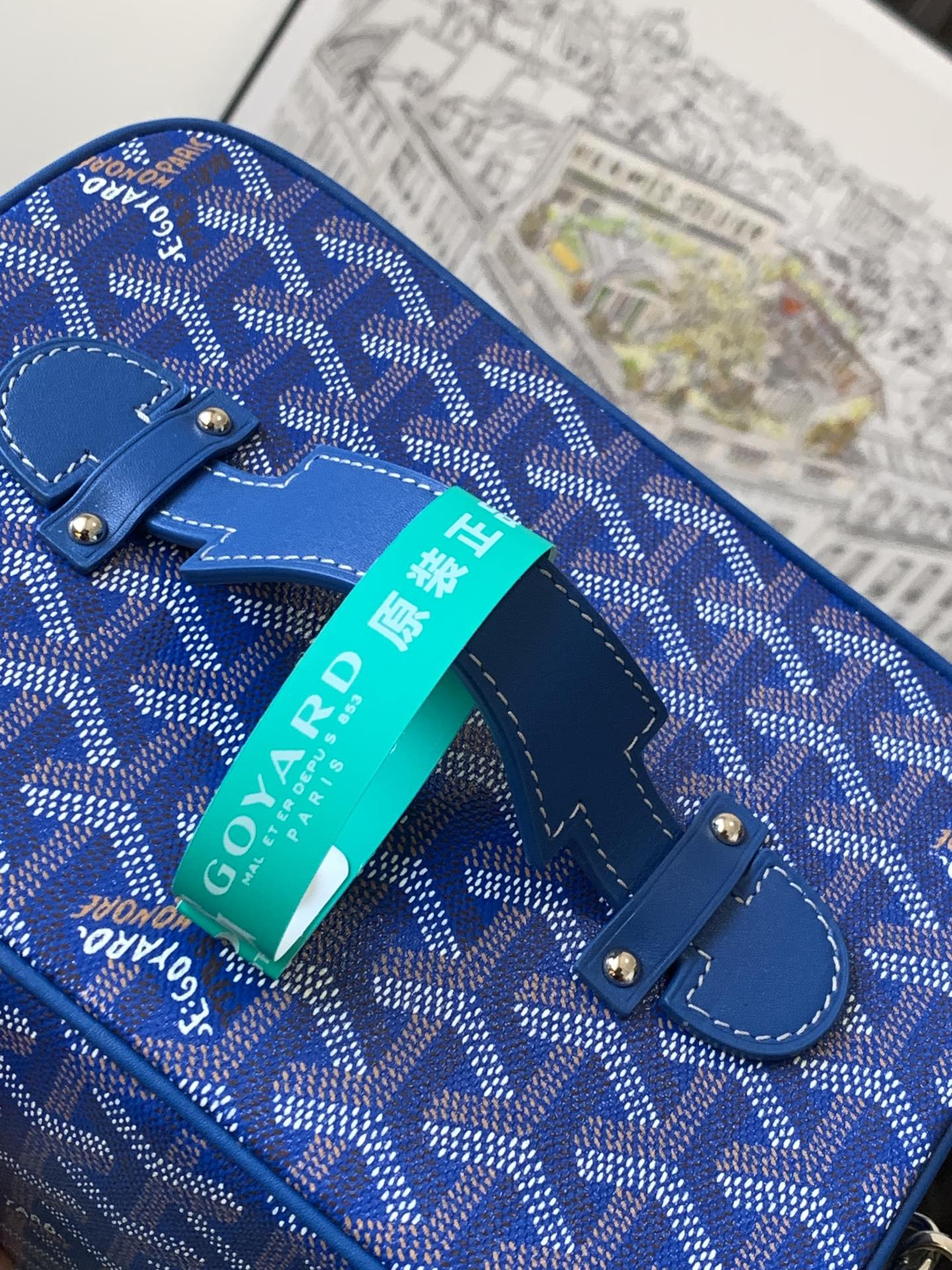 Blue patterned small bag with handle strap and metal studs, turquoise tag
