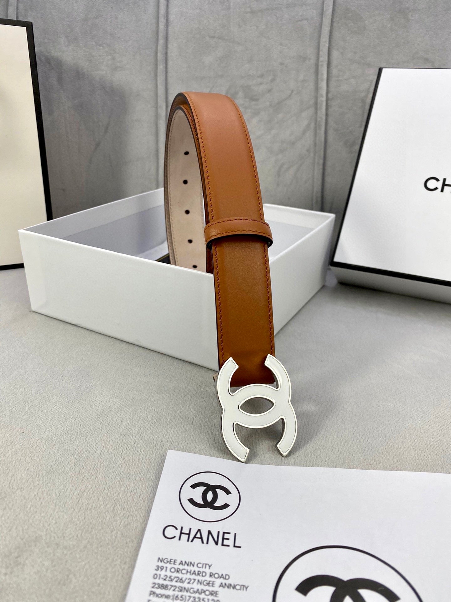 Chanel belt standing upright in box, tan leather strap with gold-tone CC buckle