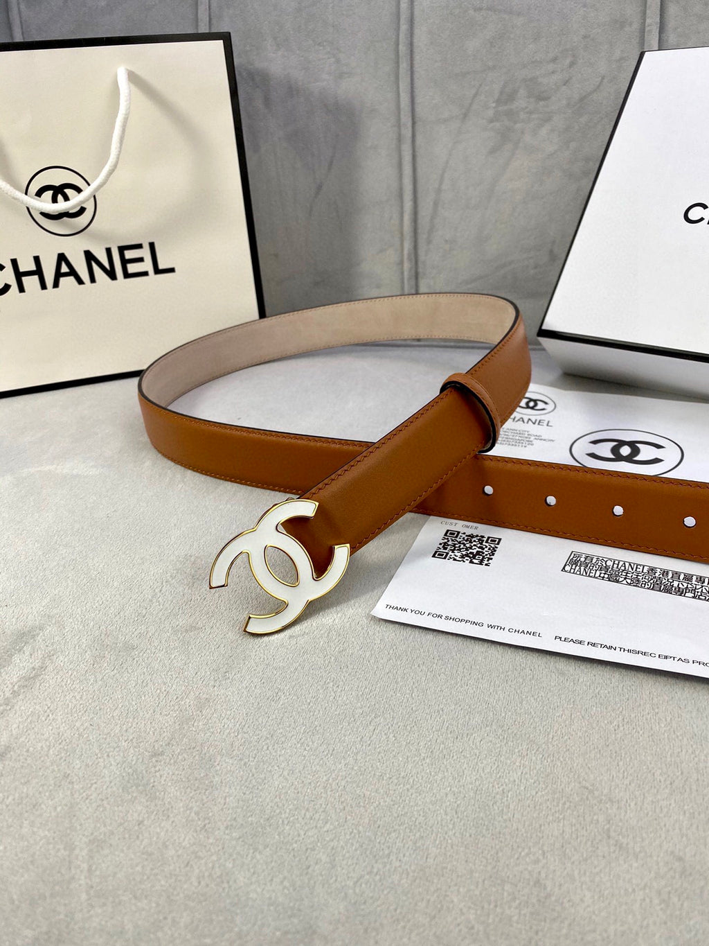 Chanel belt on tabletop, tan leather strap with gold-tone CC buckle and adjustable holes