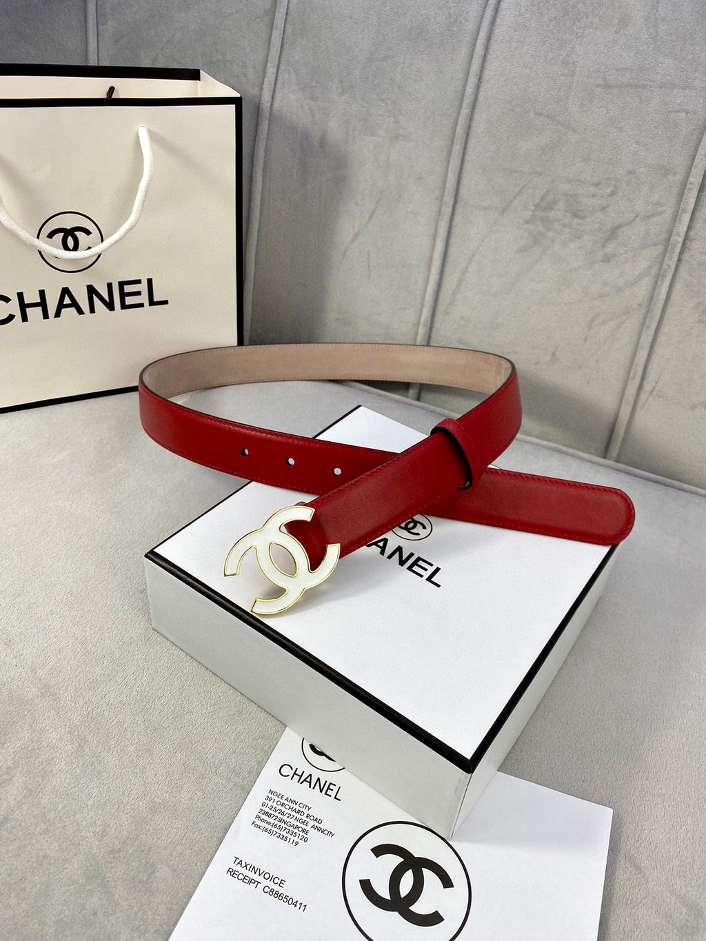 Red leather belt with gold-tone CC buckle resting on white box and papers