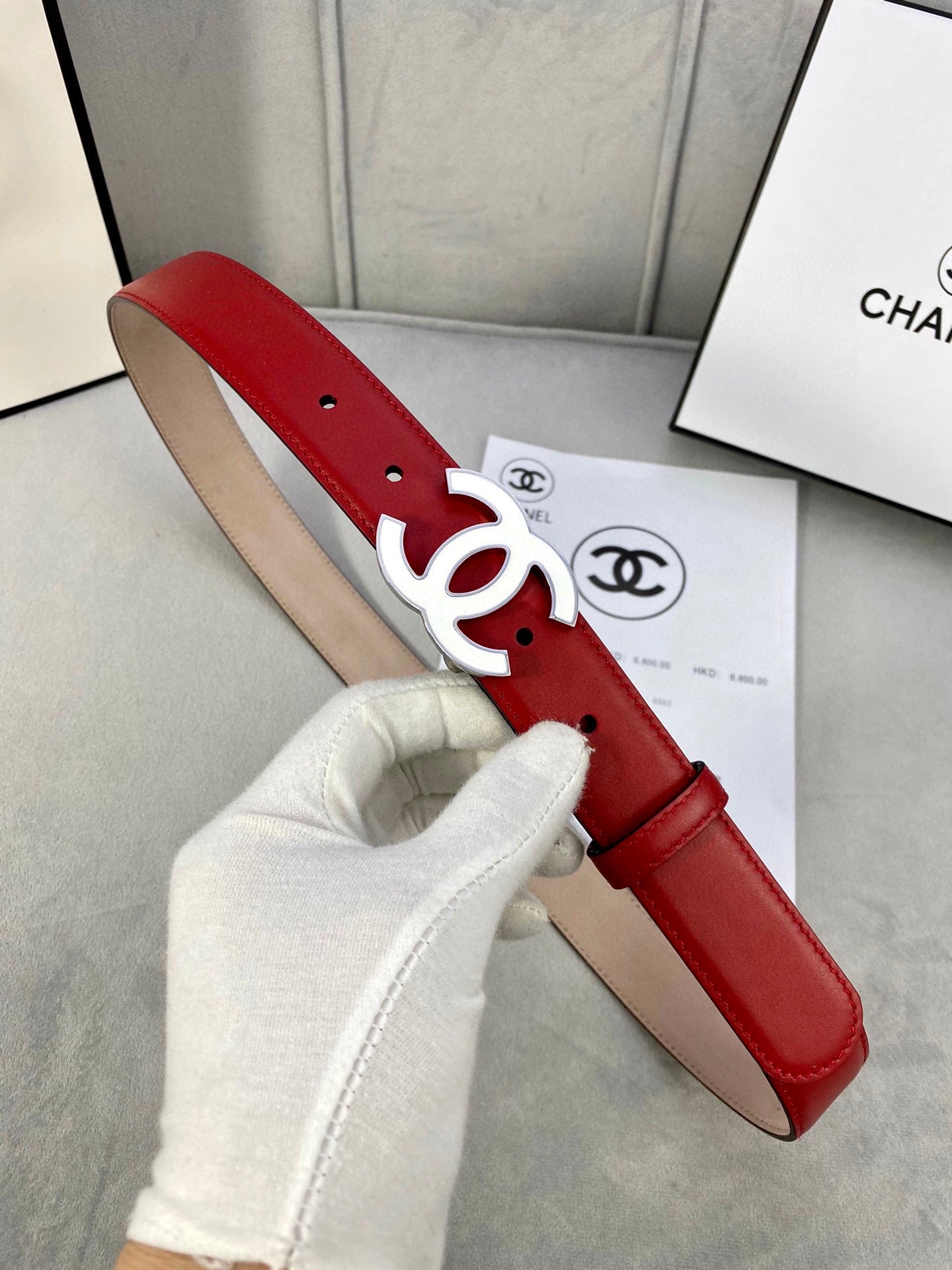 Red leather belt with gold-tone CC logo buckle held by white-gloved hand