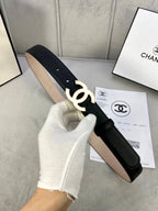 Black leather belt with gold CC buckle, held up in a white-gloved hand