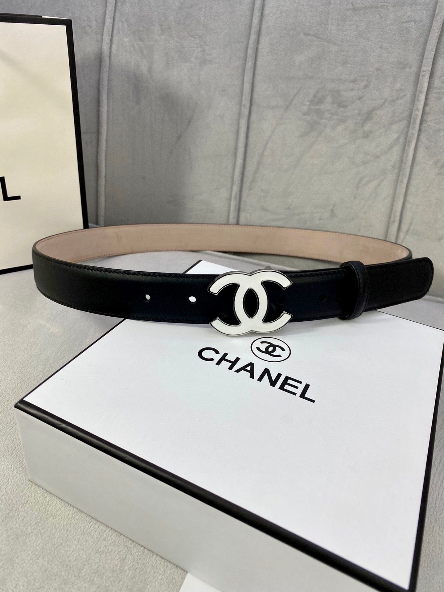 Black leather belt with gold CC buckle, laid flat on its box