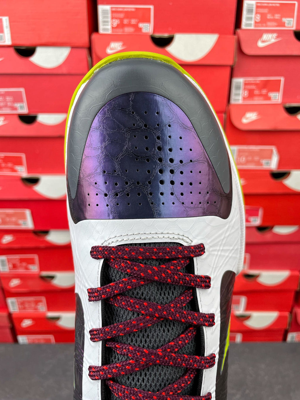 Low-top basketball shoe toe view: white upper with purple vamp and red laces