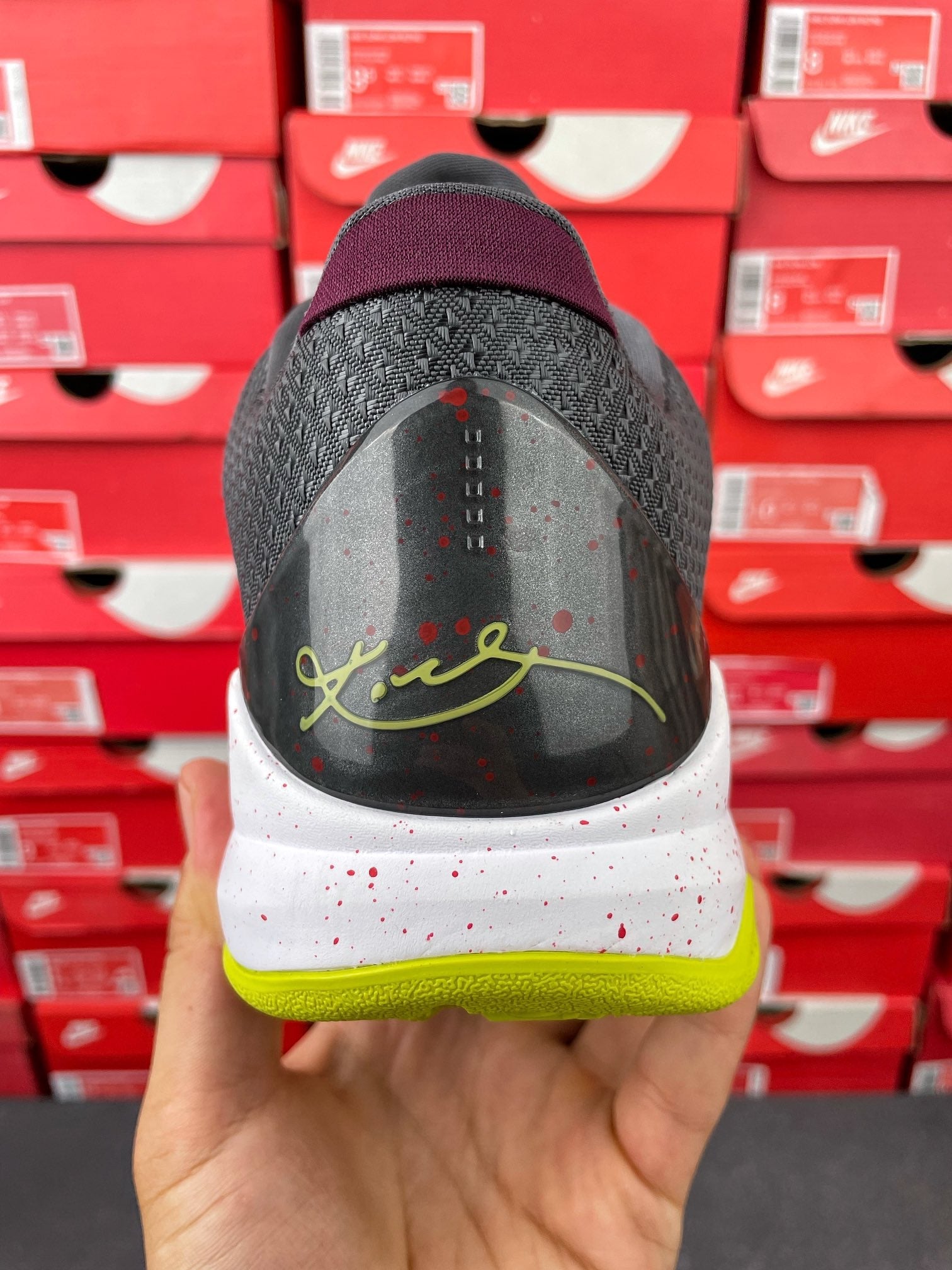 Low-top basketball shoe heel view in hand with dark upper and neon green trim
