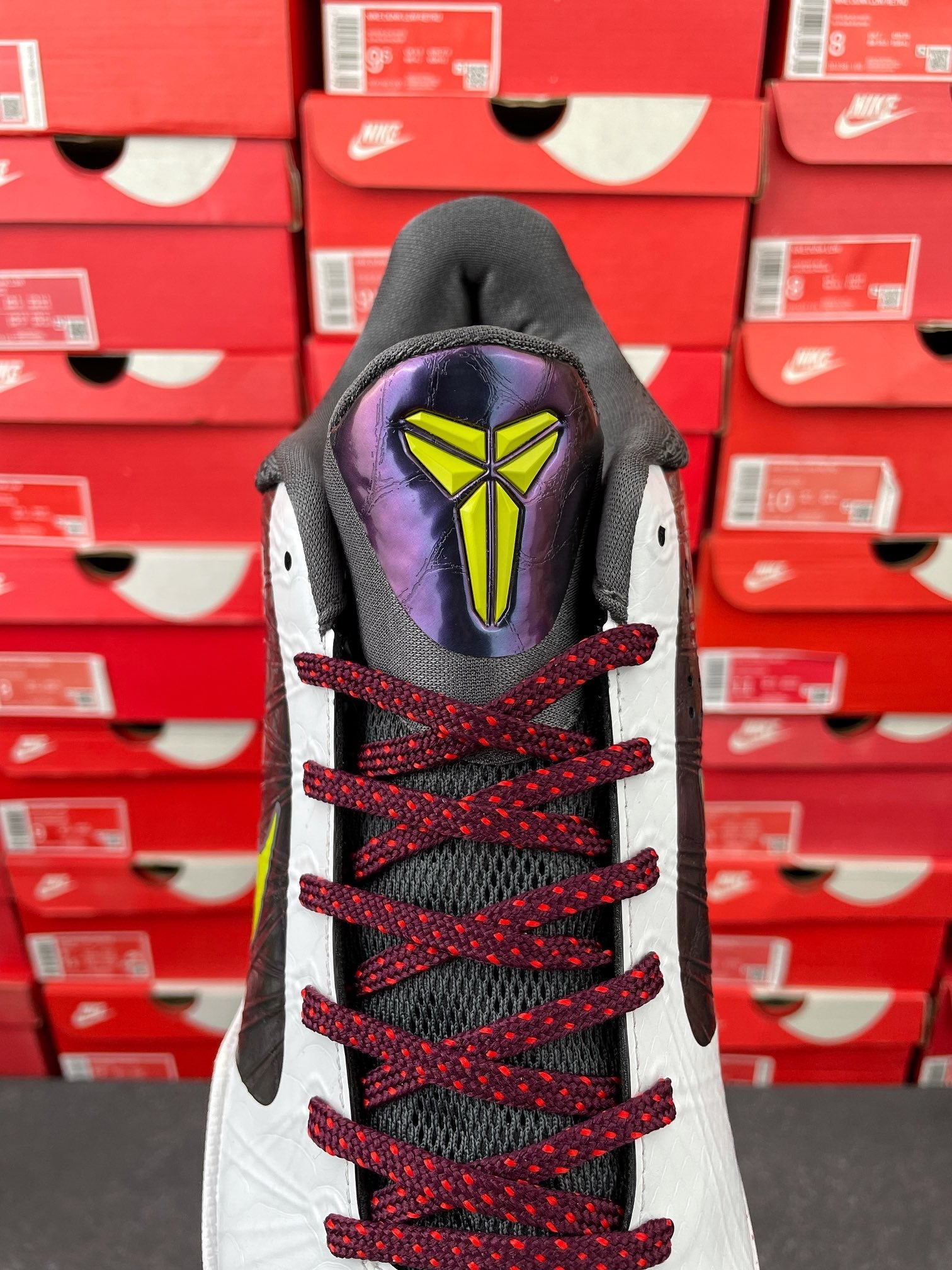 Low-top basketball shoe heel view: black collar, white sides, red laces, neon detail