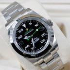Rolex watch angled view with black dial, green accents, steel bracelet