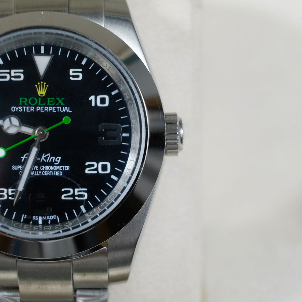 Rolex watch dial close-up with black face, green hands, steel case