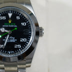 Rolex watch dial close-up with black face, green hands, steel case