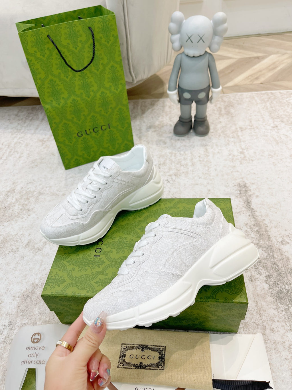 White Gucci lace-up sneakers on green box, pair angled with hand holding one