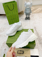 White Gucci lace-up sneakers on green box, pair angled with hand holding one