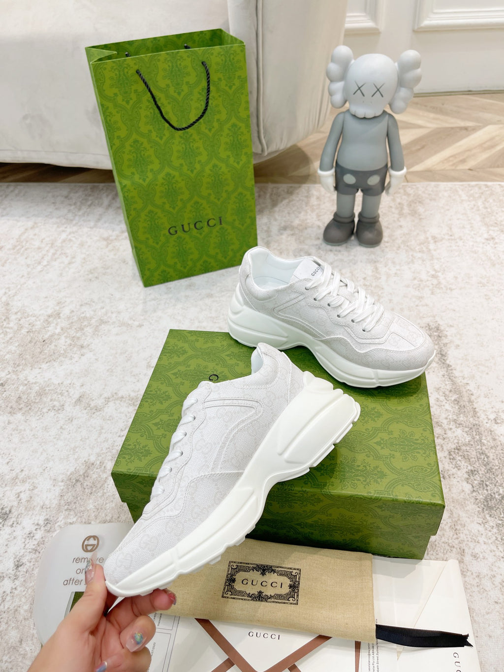 White Gucci lace-up sneakers on green box, one held in hand near tag