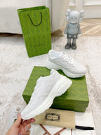 White Gucci lace-up sneakers on green box, one held in hand near tag