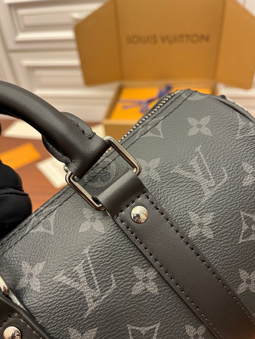 Men's Louis Vuitton monogram bag close-up of strap buckle and leather tab, dark