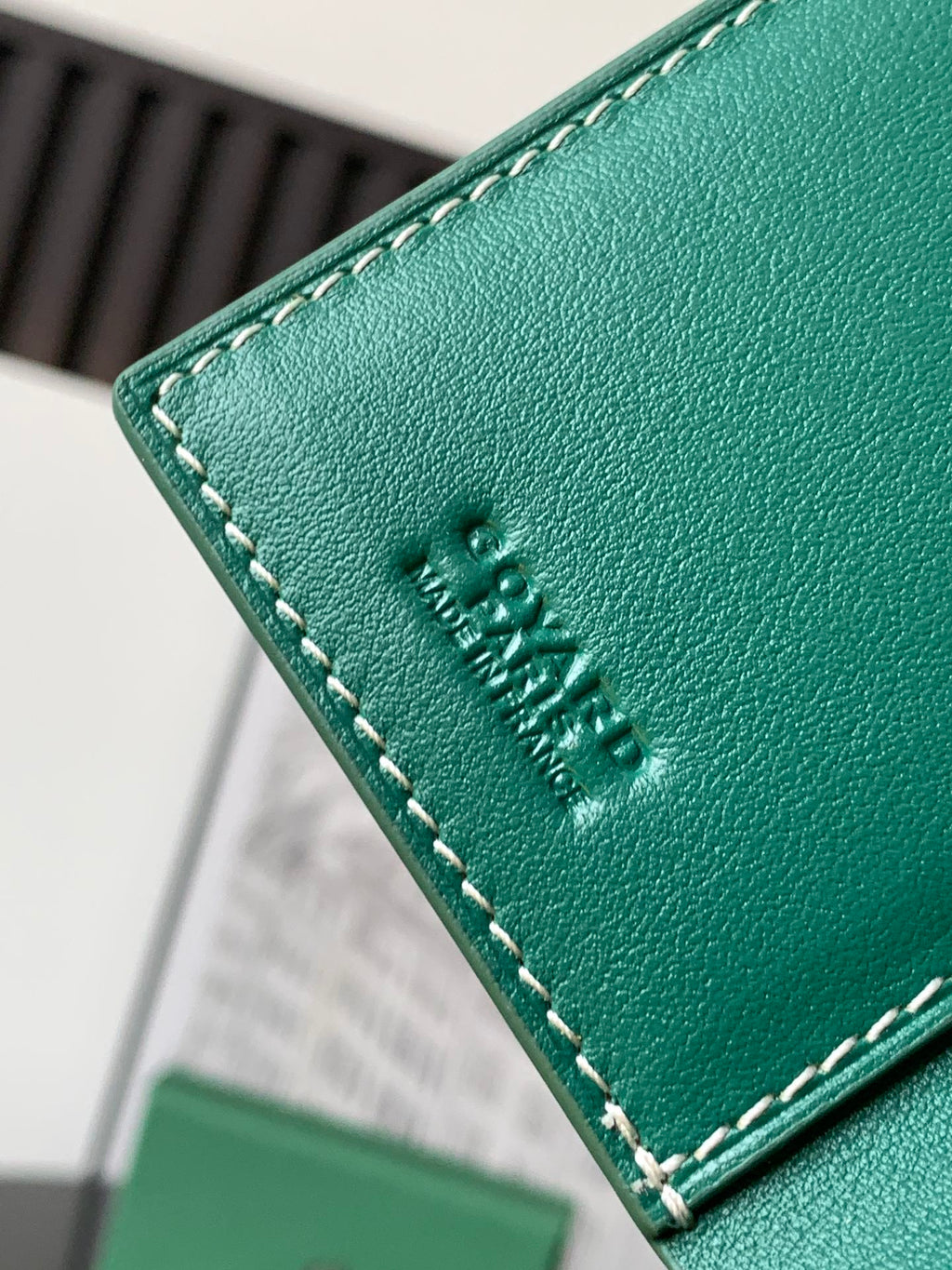 Green leather card holder edge with embossed logo and contrast stitching