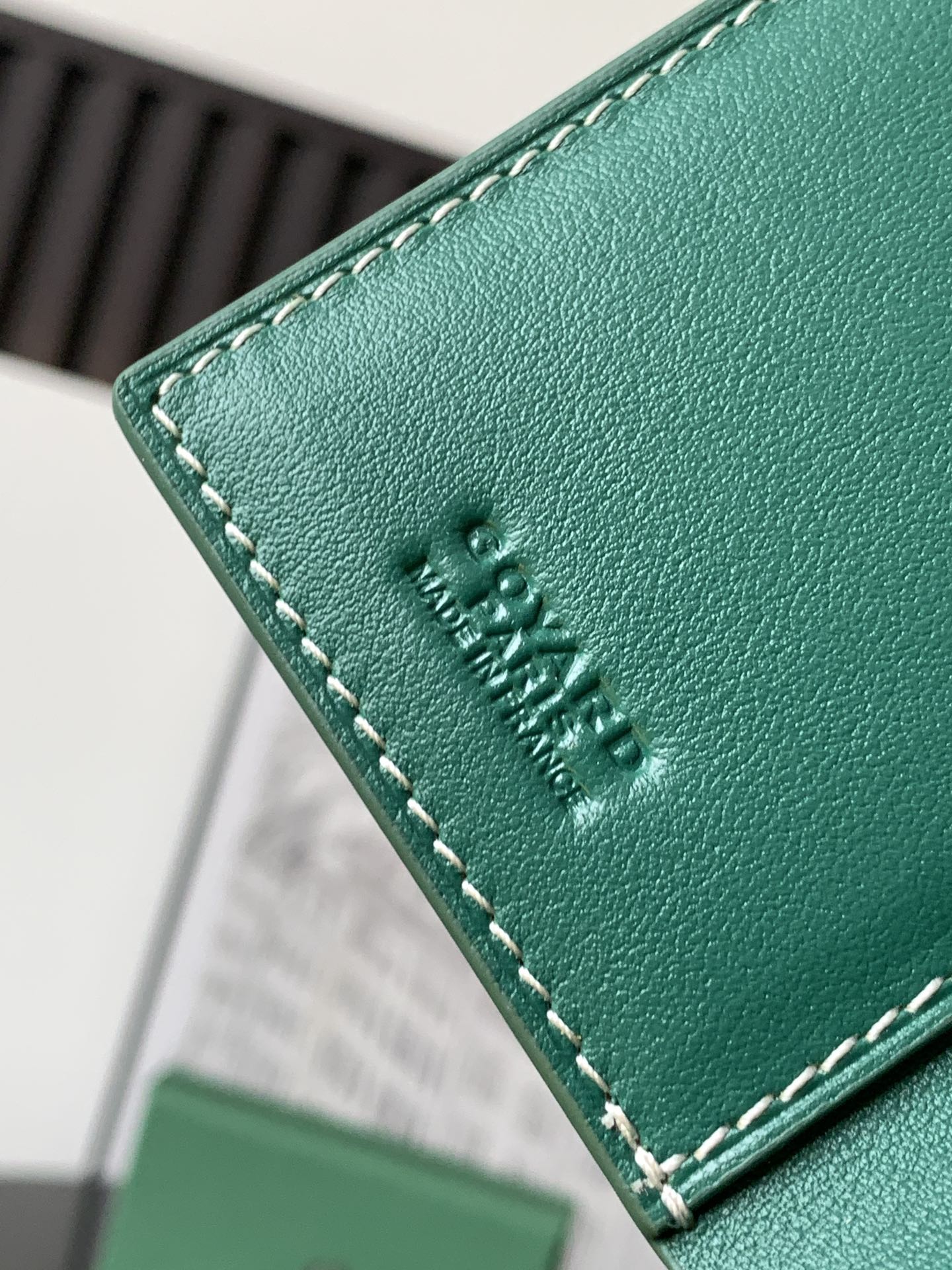 Green leather card holder edge with embossed logo and contrast stitching