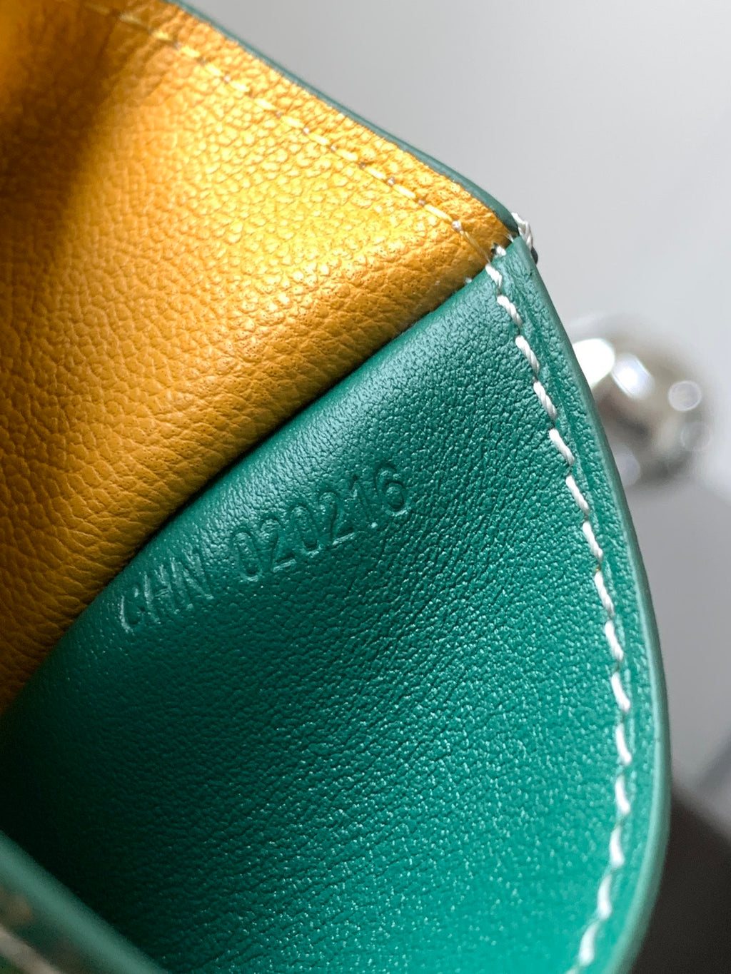 Teal and yellow leather small bag close-up with embossed logo and white stitching.