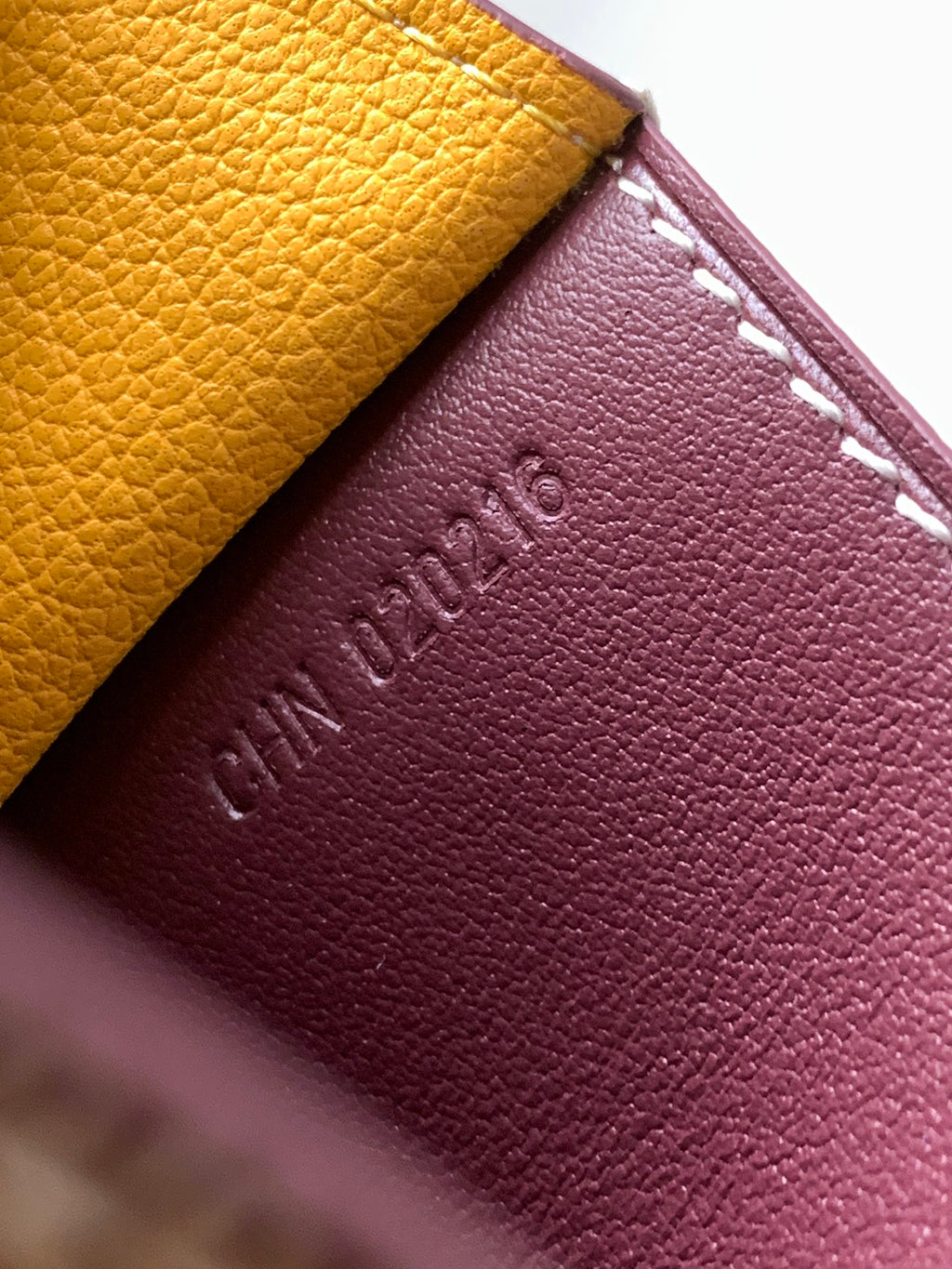 Maroon leather small bag with embossed text and white stitching