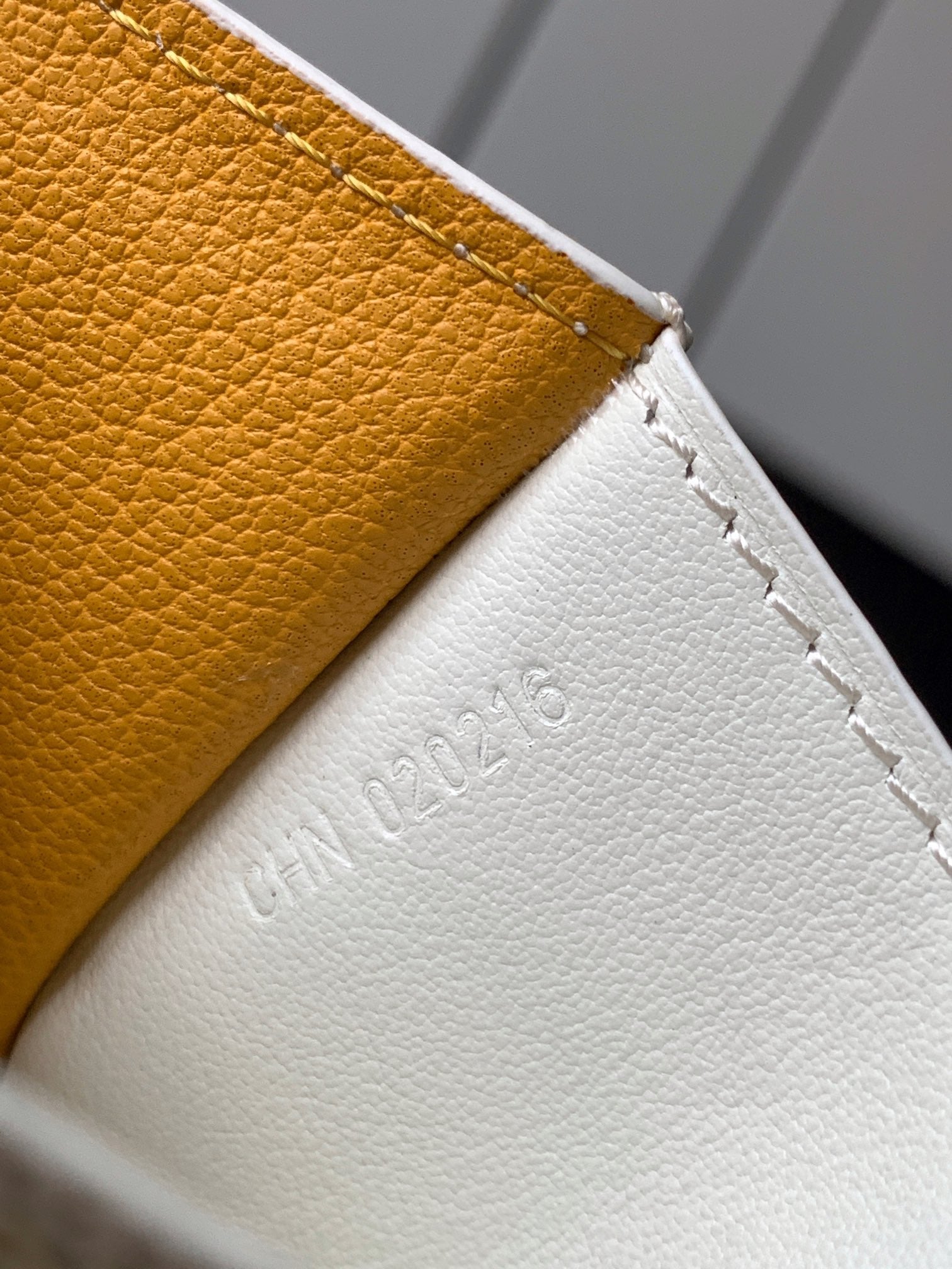 Small bag edge with embossed text on white leather, yellow trim and stitched seam