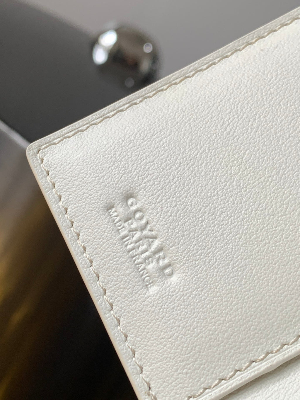 Small bag corner with embossed logo on white textured leather and stitched edge