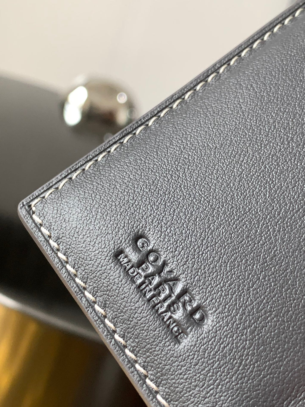 Small bag corner in dark gray pebbled leather with embossed logo and contrast stitching.