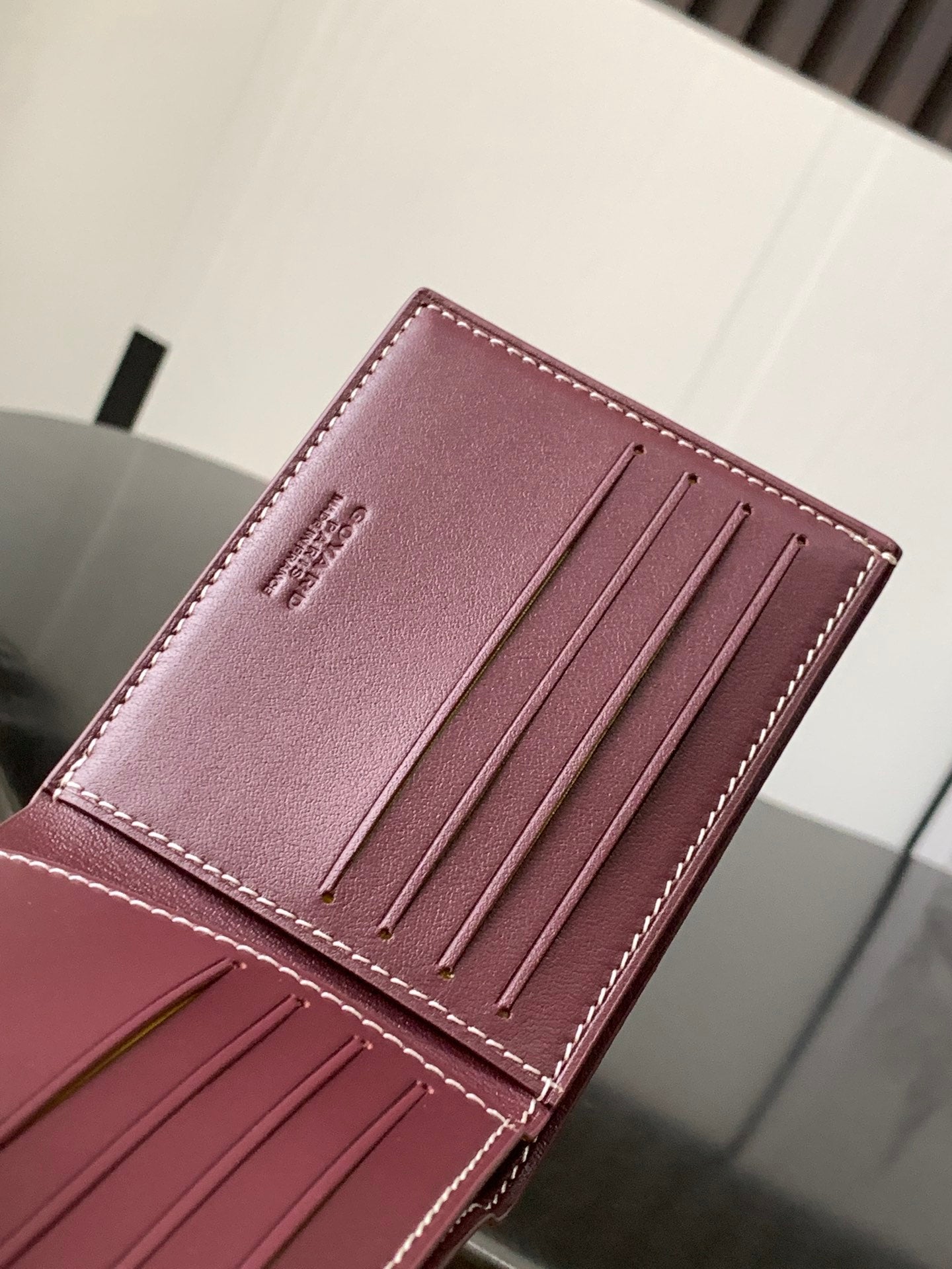 Burgundy leather card holder showing four card slots and logo stamp