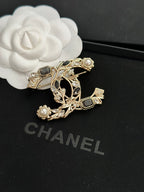 Ornate gold-tone brooch with faux pearls and dark gemstone accents, leaf-and-vine design