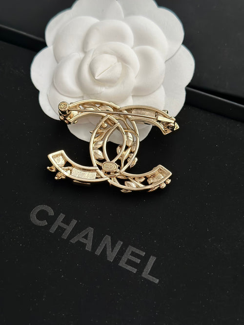 Gold-tone brooch with pearl details and dark gemstone accents, ornate curved design