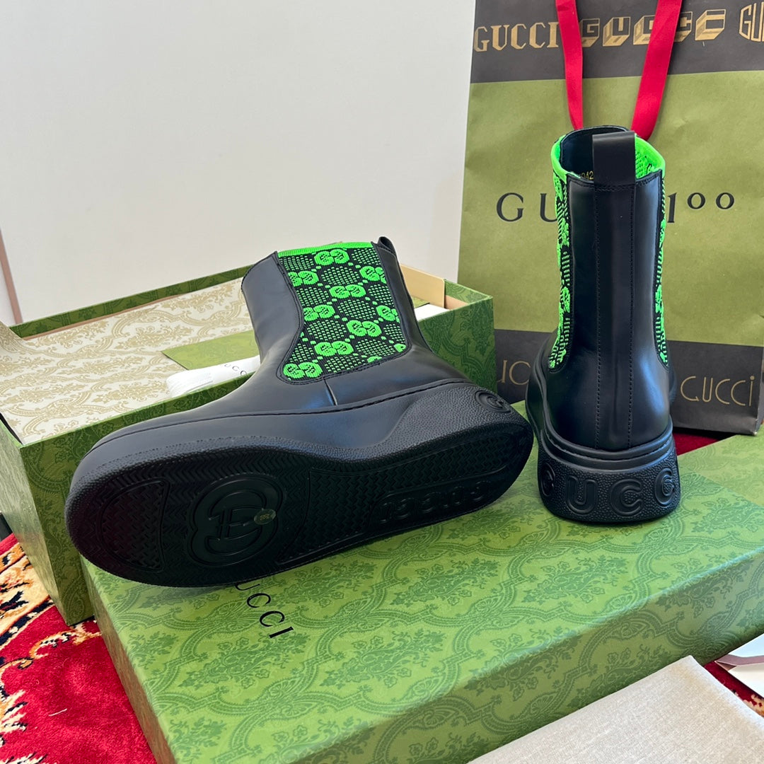 Black Chelsea boots with neon green GG-pattern elastic, rubber sole visible.