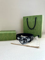Gucci belt resting on cloth: dark navy leather with white trefoil emblems and metal buckle