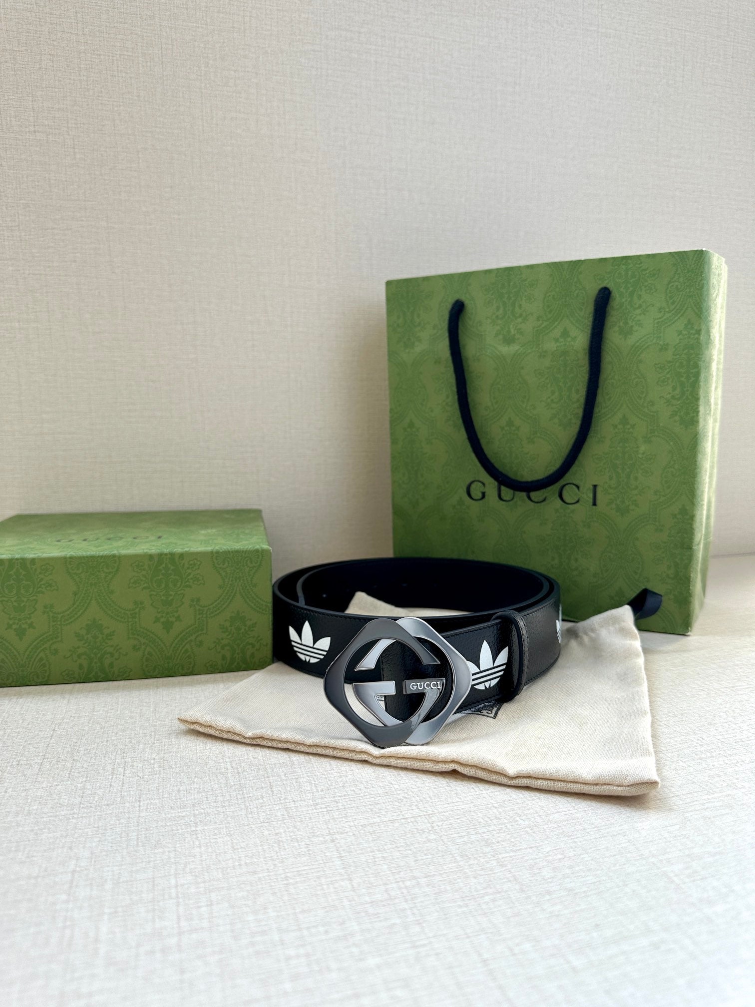 Gucci belt resting on cloth: dark navy leather with white trefoil emblems and metal buckle