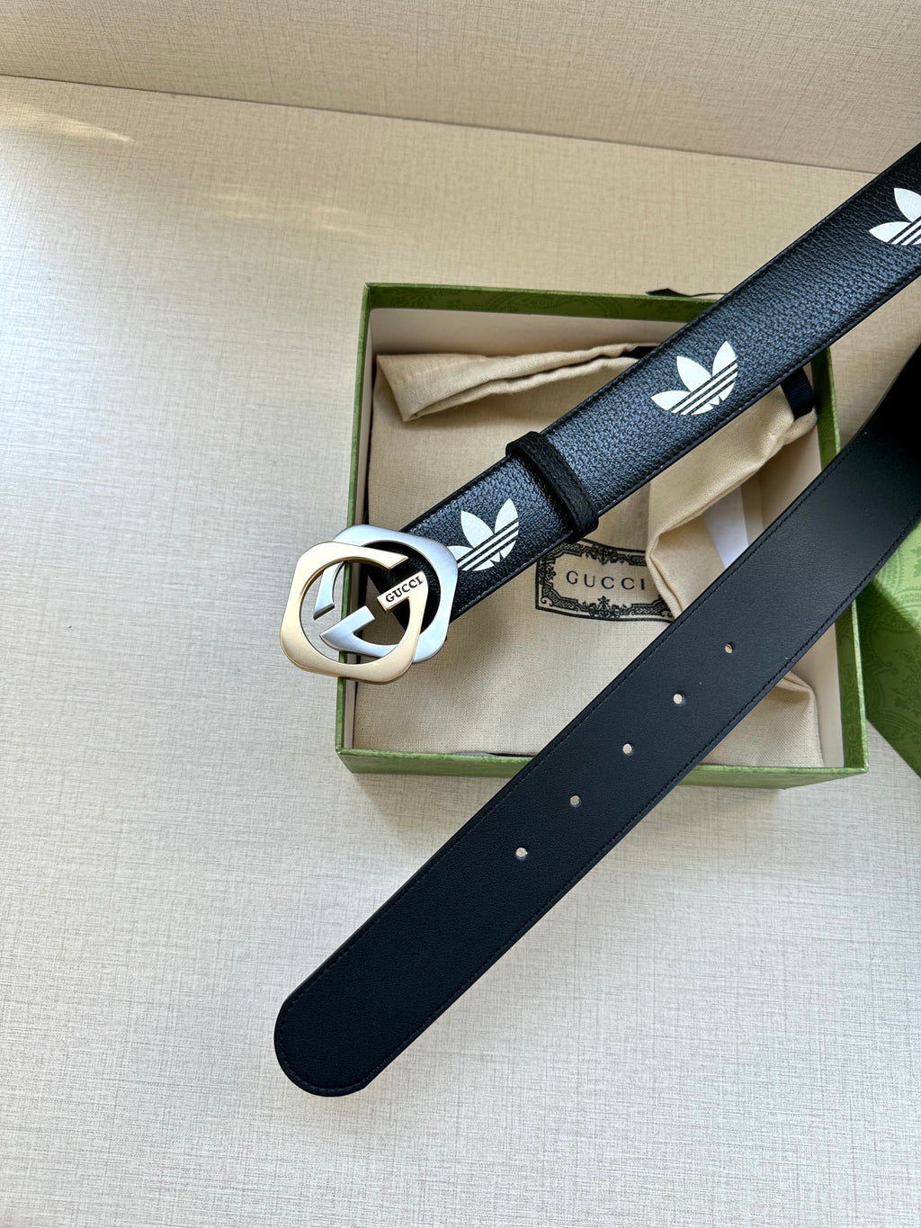 Gucci belt with dark navy strap, white trefoil logos, and round buckle on box display