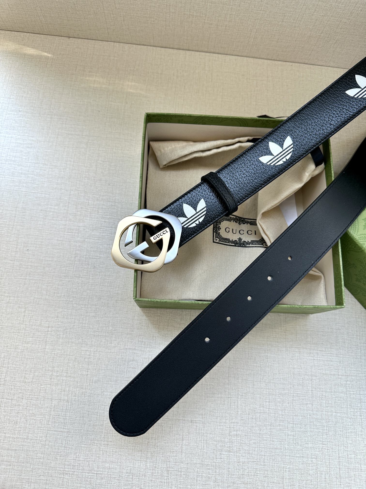 Gucci belt with dark navy strap, white trefoil logos, and round buckle on box display