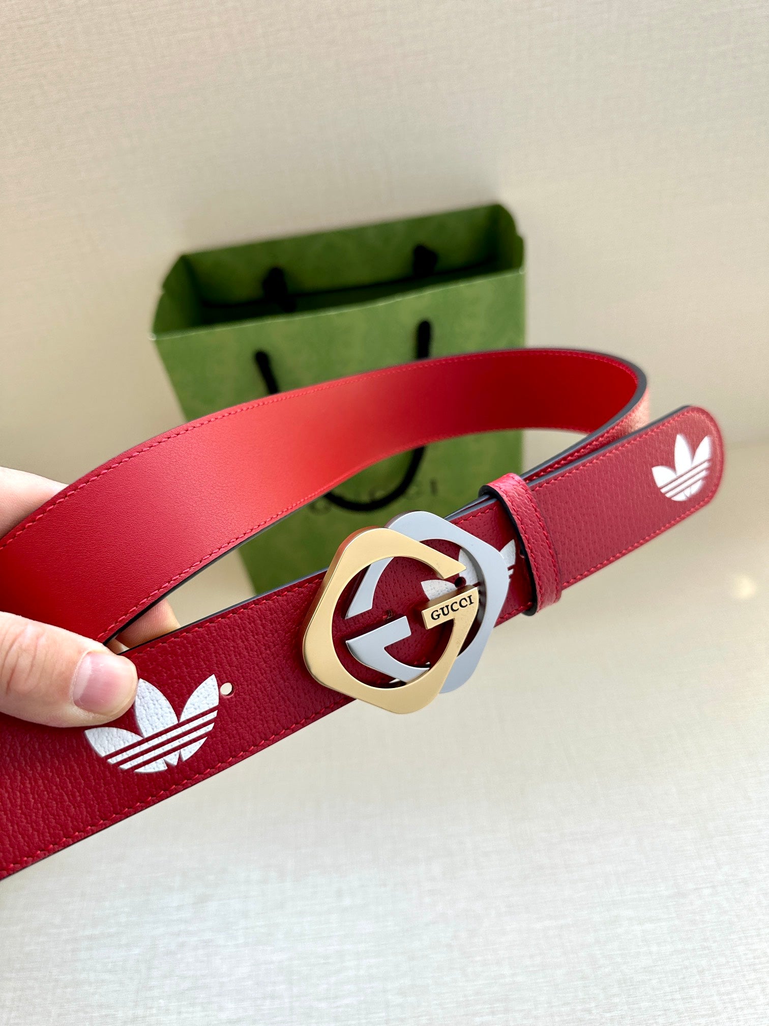 Red Gucci belt with white trefoil print and gold-trimmed logo buckle close-up