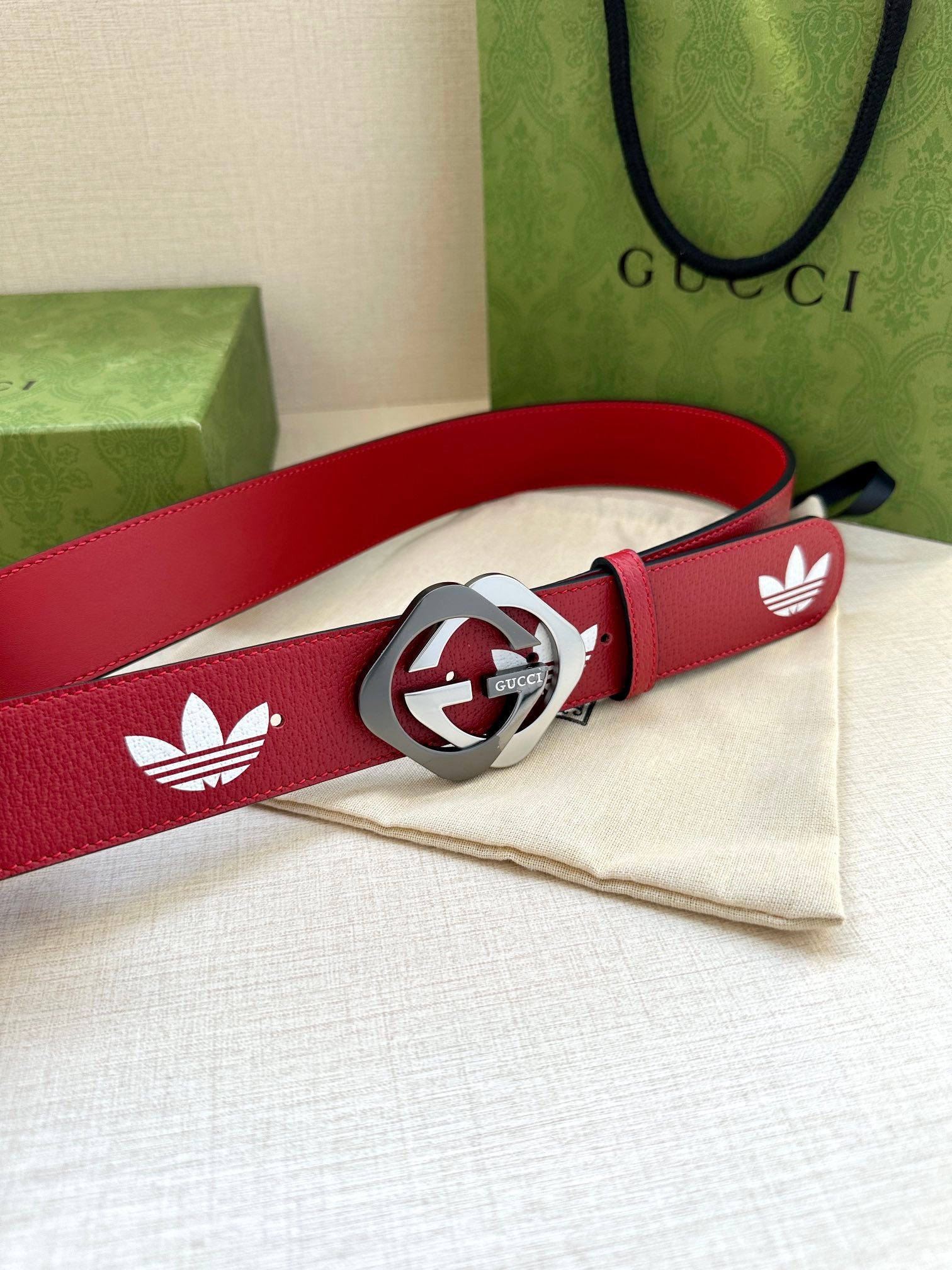 Red Gucci belt with white trefoil print and silver-tone circular logo buckle
