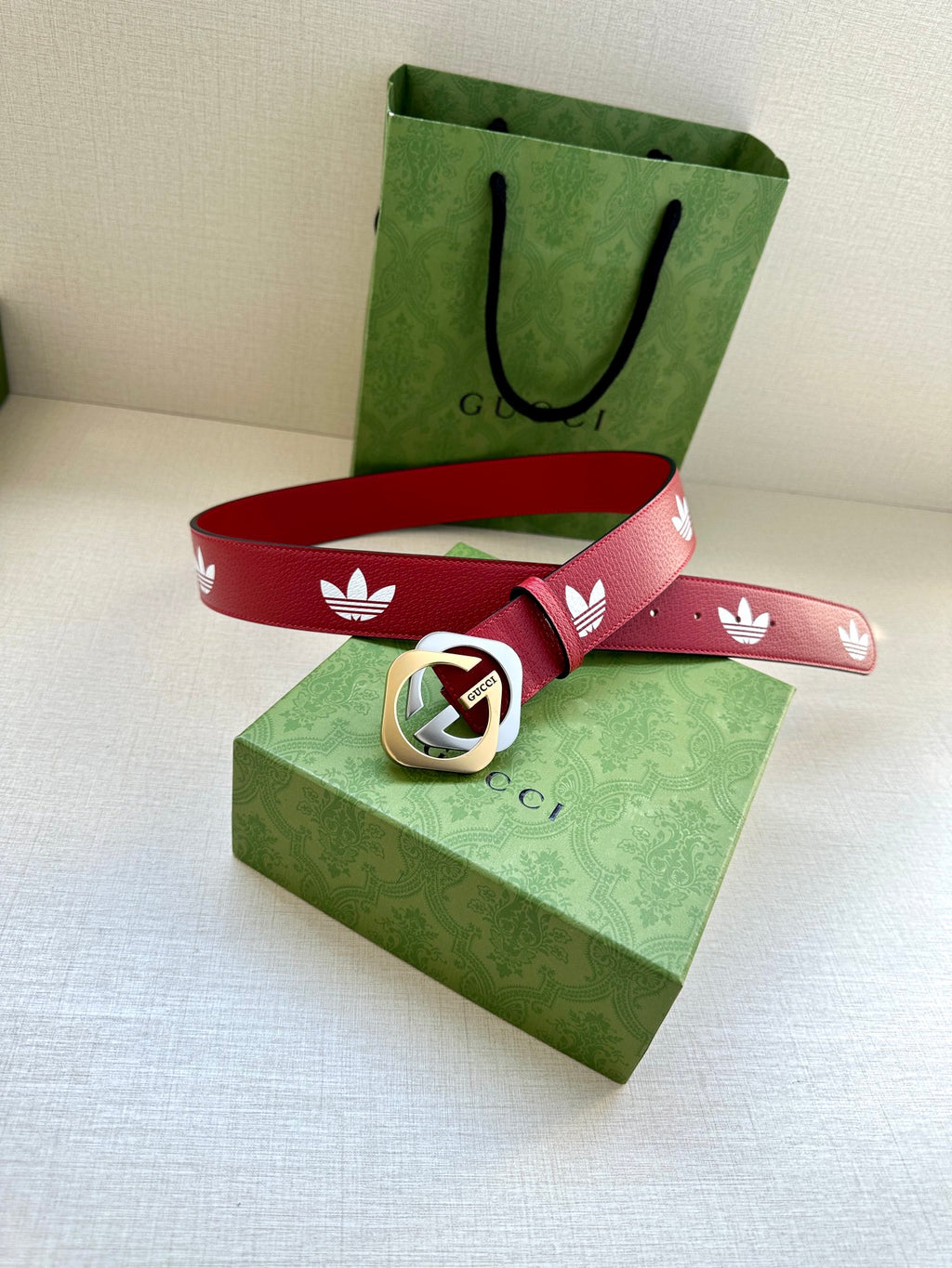 Red Gucci belt with white trefoil print and gold-and-silver logo buckle on box