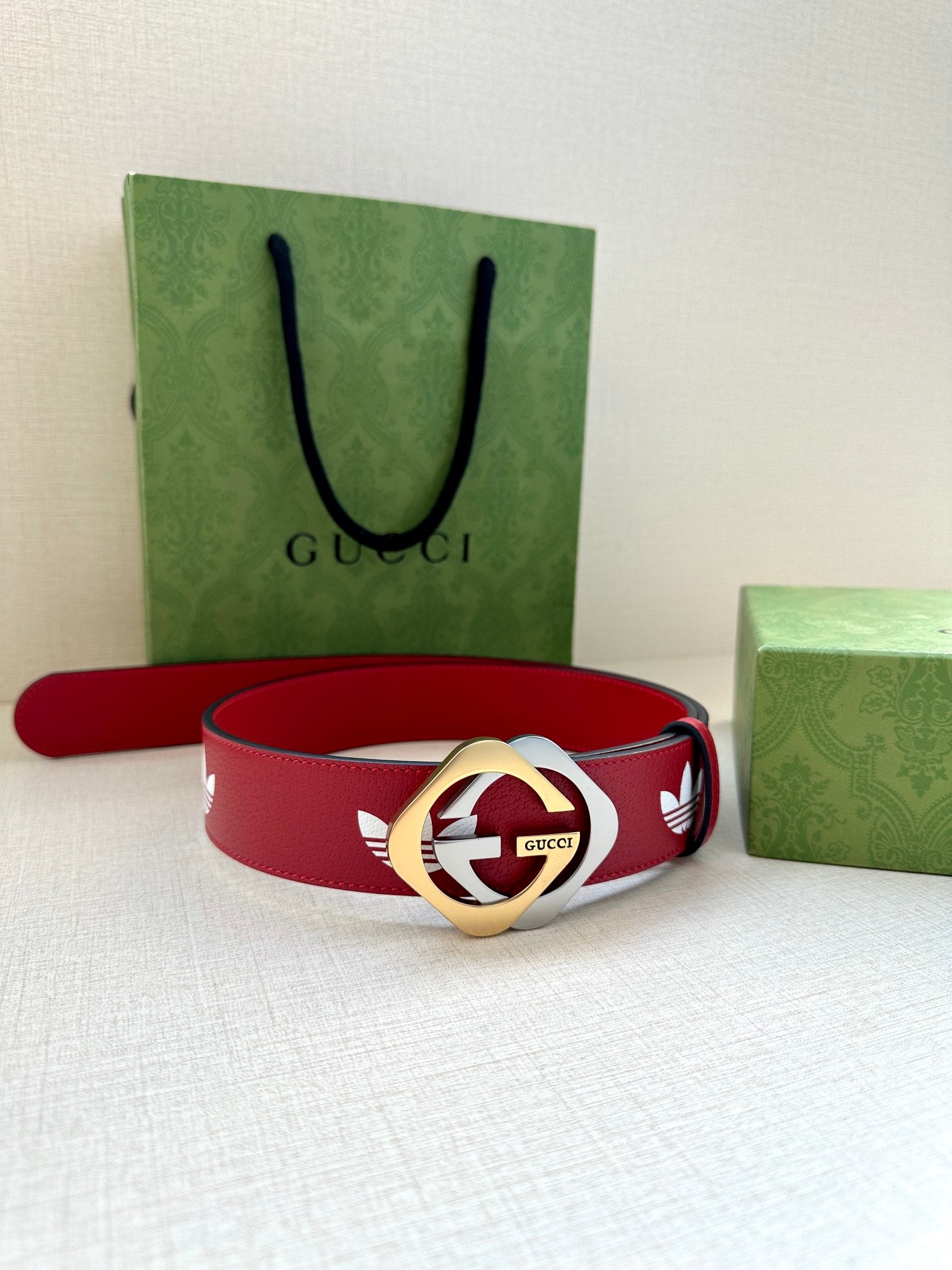 Red Gucci belt with white trefoil pattern and gold-and-silver round logo buckle