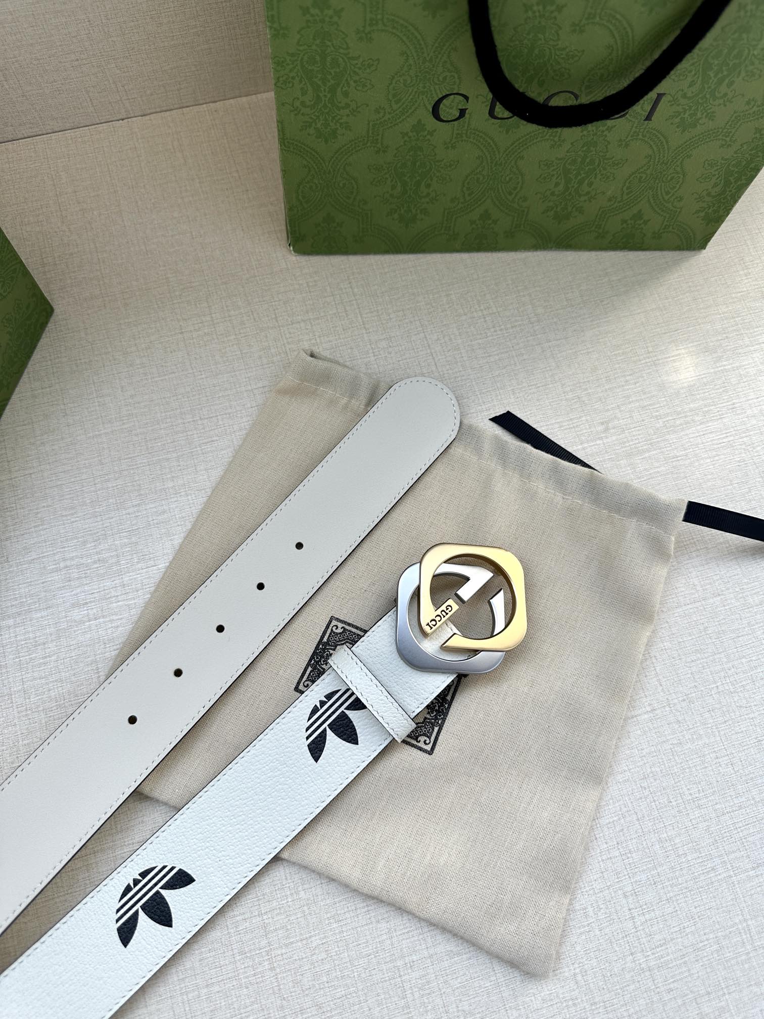 Gucci belt with white leather strap, black logo print, and gold buckle on paper packaging