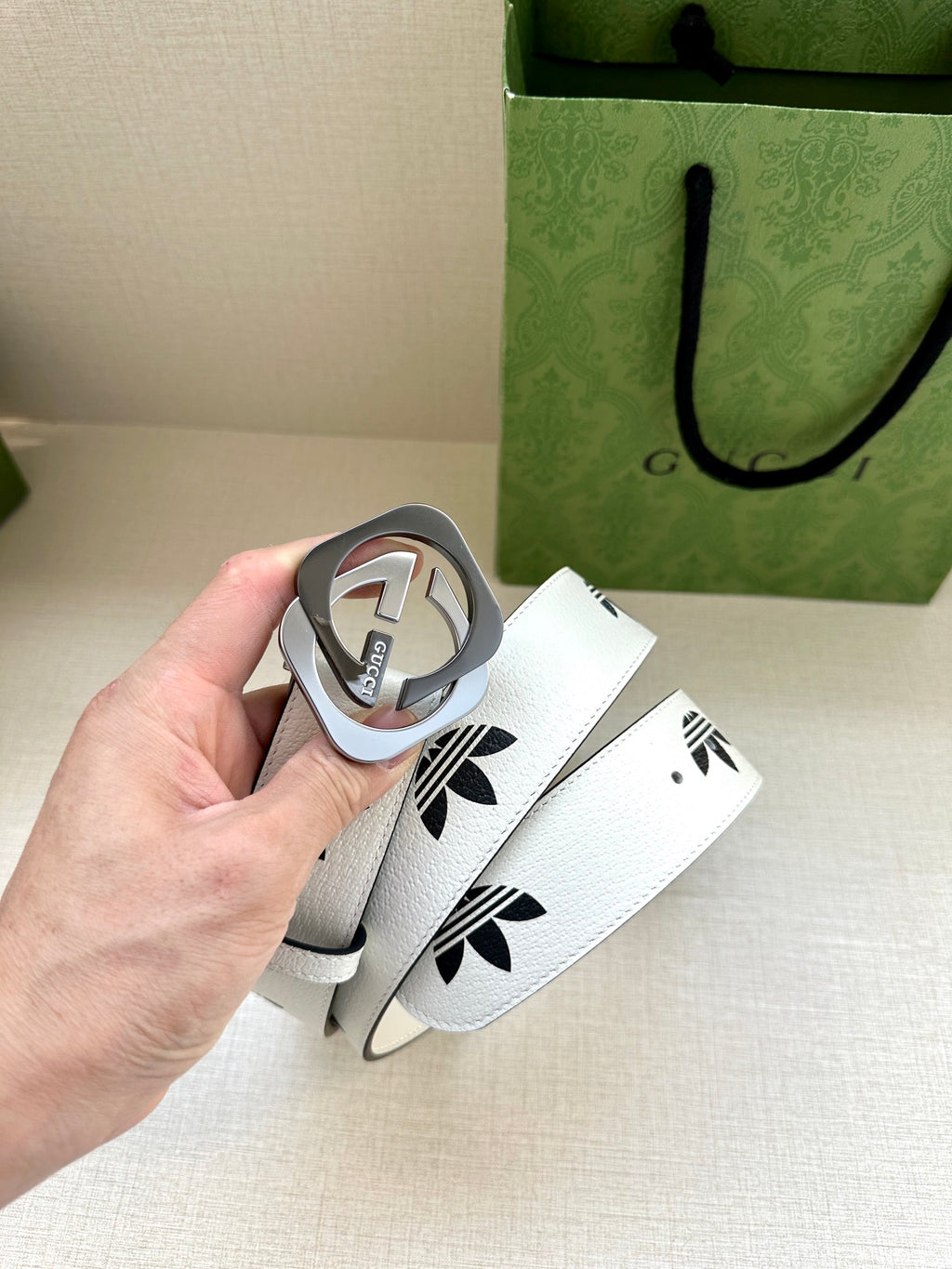 Gucci belt buckle detail with white strap and black logo print, held in hand