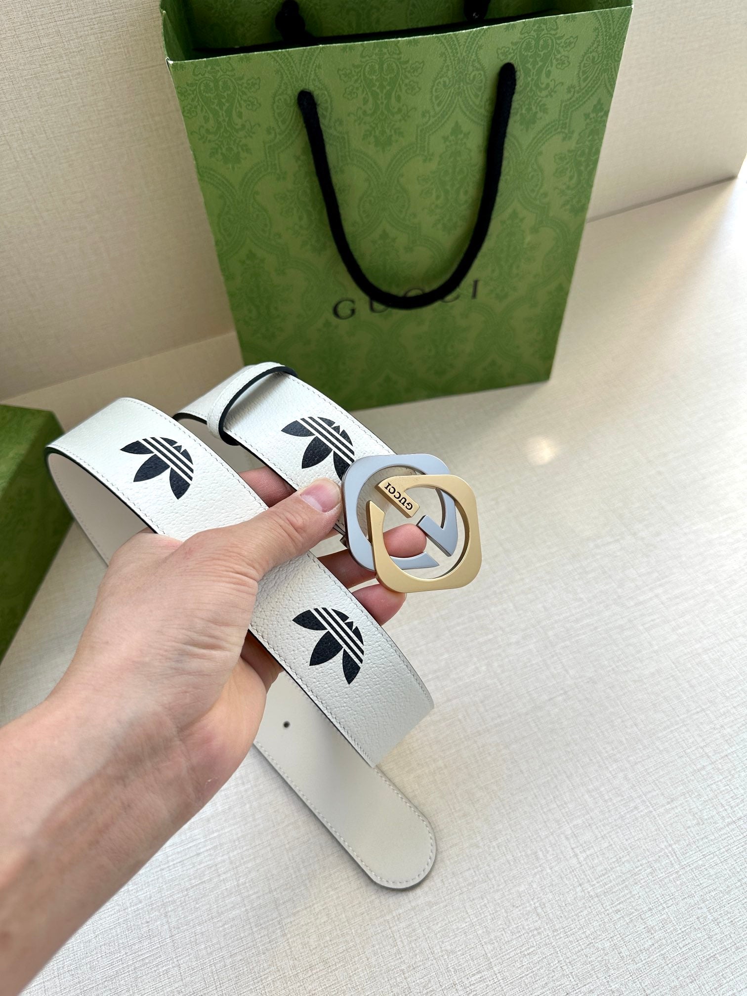 Gucci belt in white leather with black logo print and gold-tone buckle, flat lay