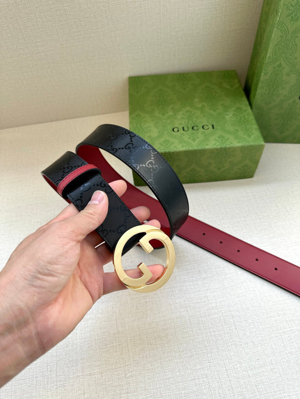 Gucci belt on hand: dark monogram leather with gold-toned G buckle and red underside.