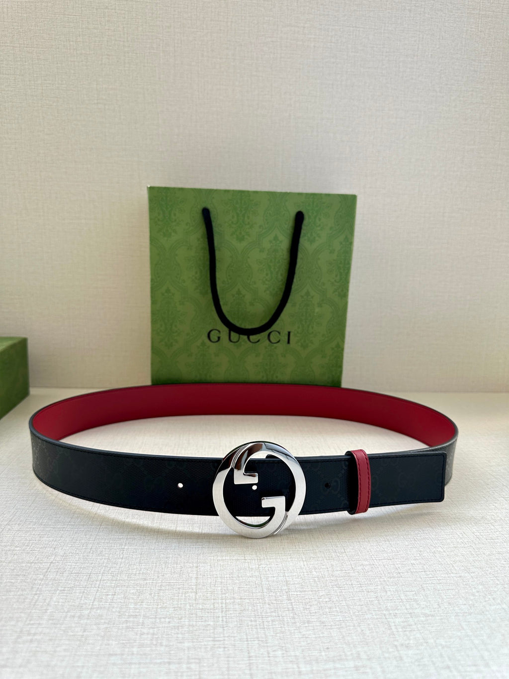 Gucci belt laid flat: dark strap with round silver G buckle and narrow red stripe.