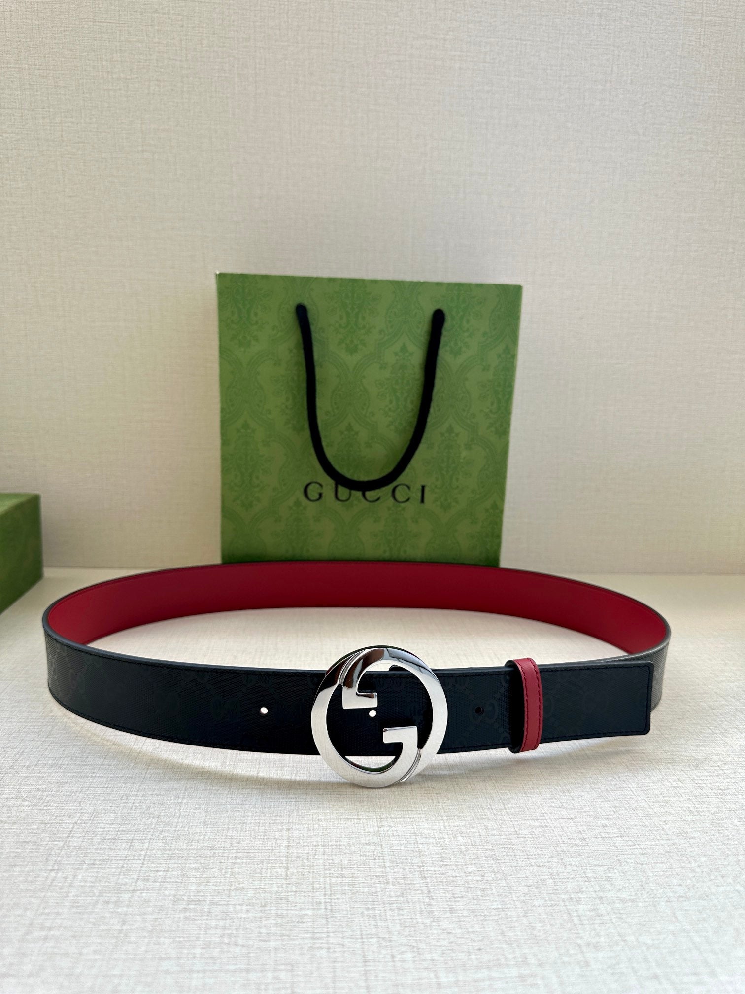 Gucci belt laid flat: dark strap with round silver G buckle and narrow red stripe.