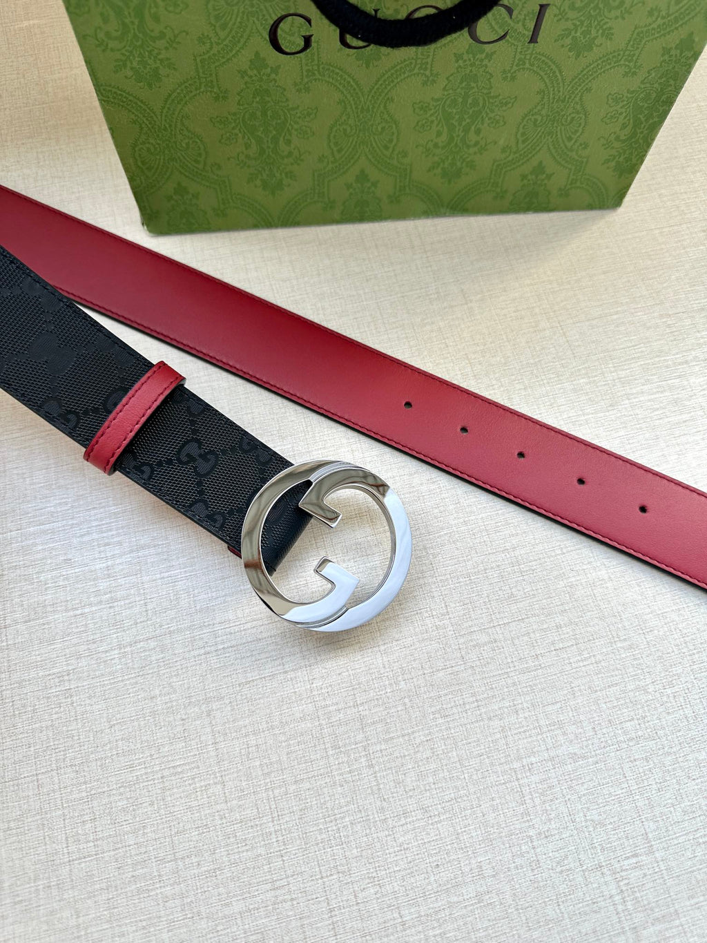 Gucci belt top view: dark monogram strap with red underside, round silver G buckle.
