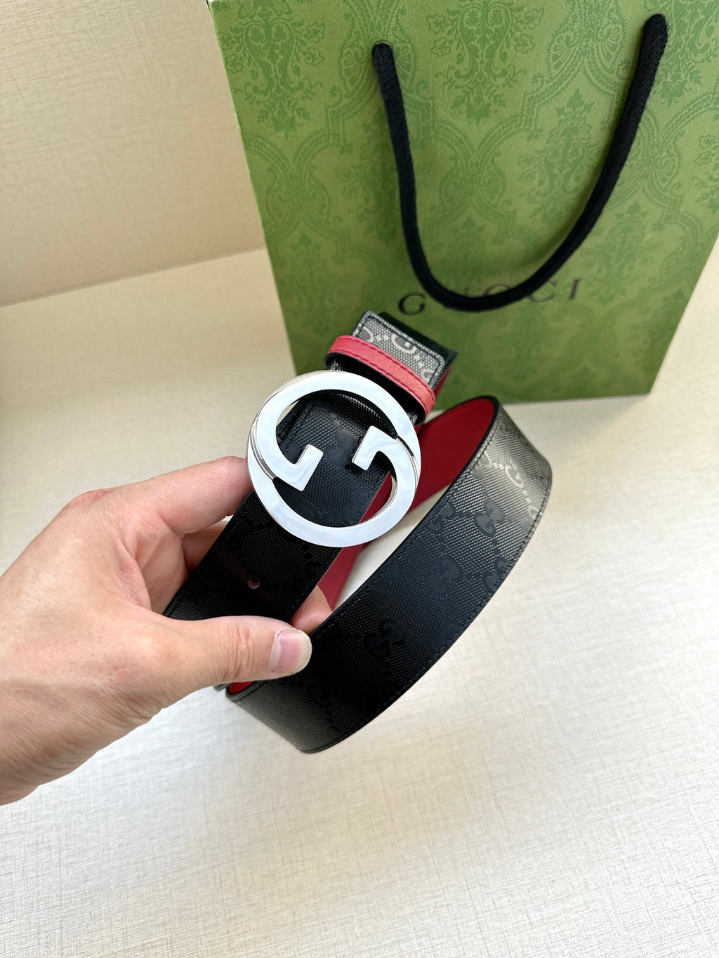 Gucci belt close-up in hand: dark monogram strap with silver-toned G buckle and red edge.