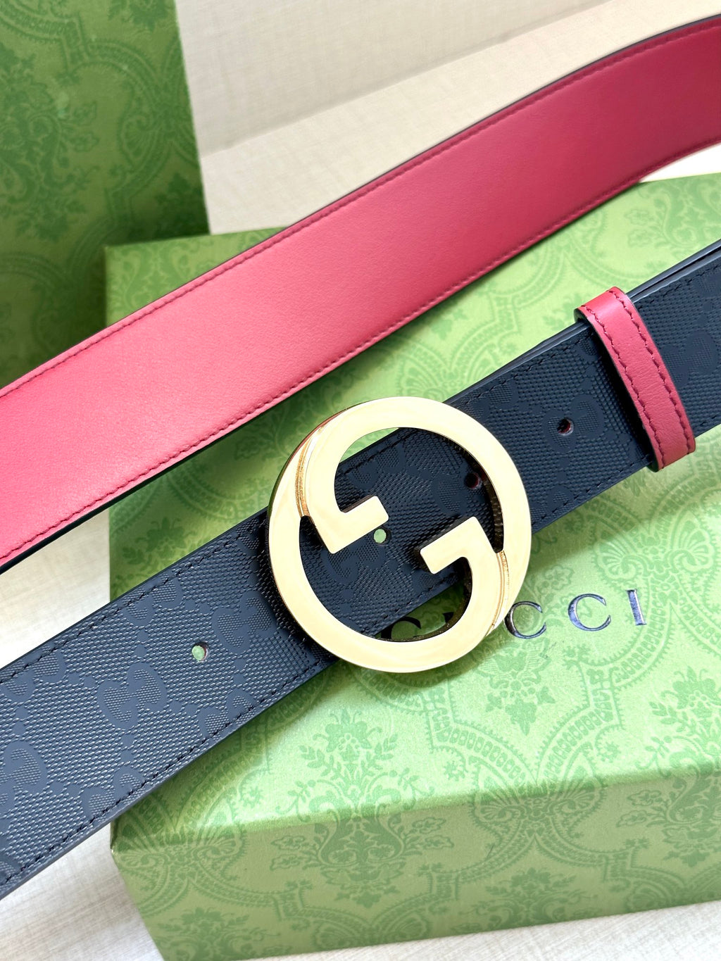 Gucci belt close-up: dark monogram strap with pink edge, large gold-toned G buckle.
