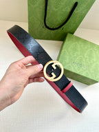 Gucci belt with dark monogram strap, gold-toned round G buckle, red underside trim.