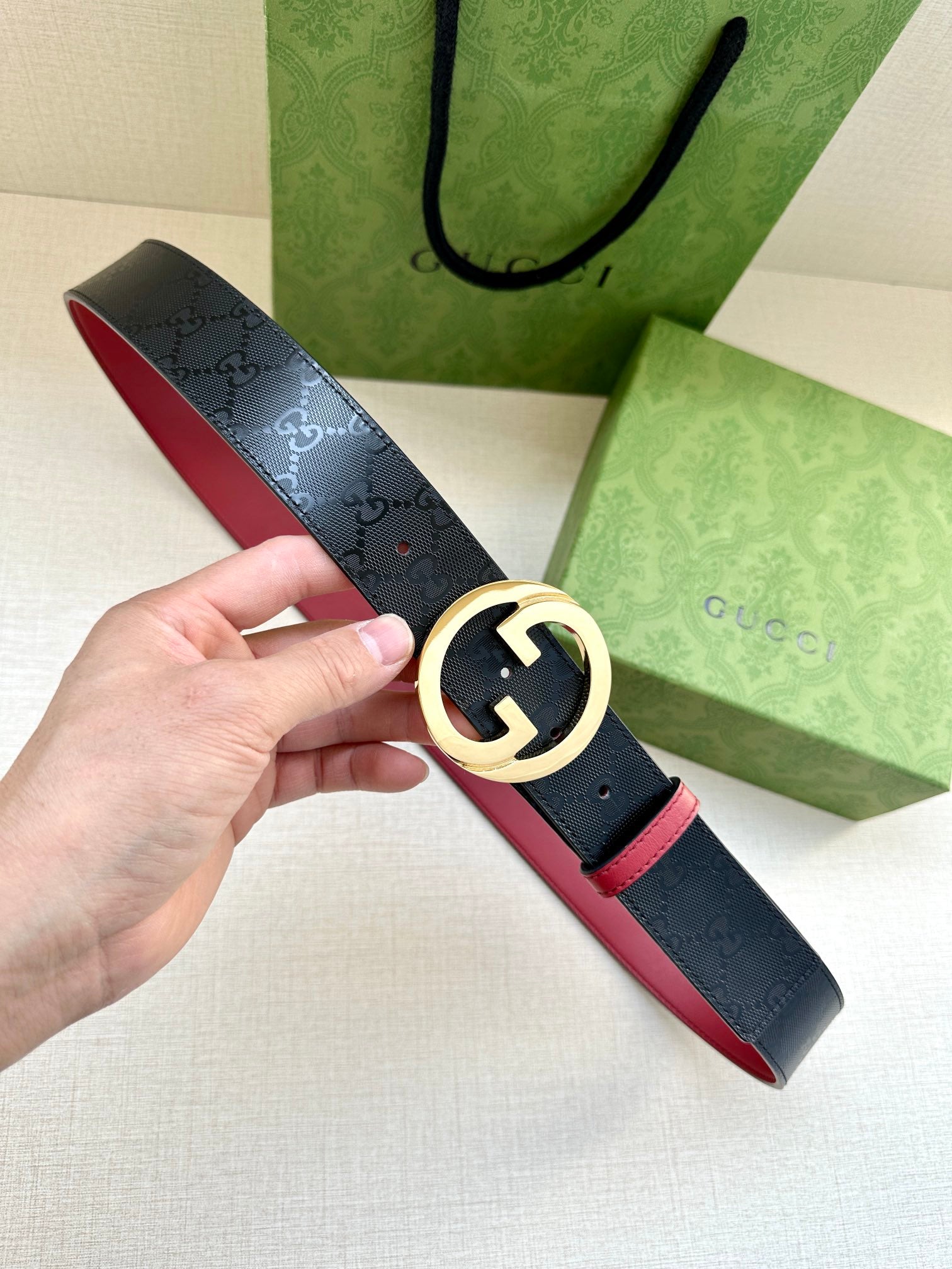 Gucci belt with dark monogram strap, gold-toned round G buckle, red underside trim.