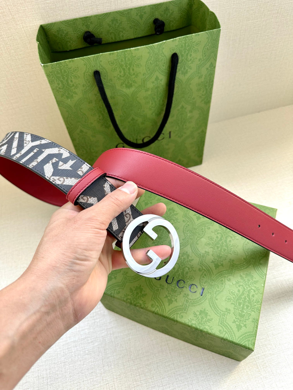 Gucci belt with navy monogram webbing and silver-tone GG buckle on red leather strap.