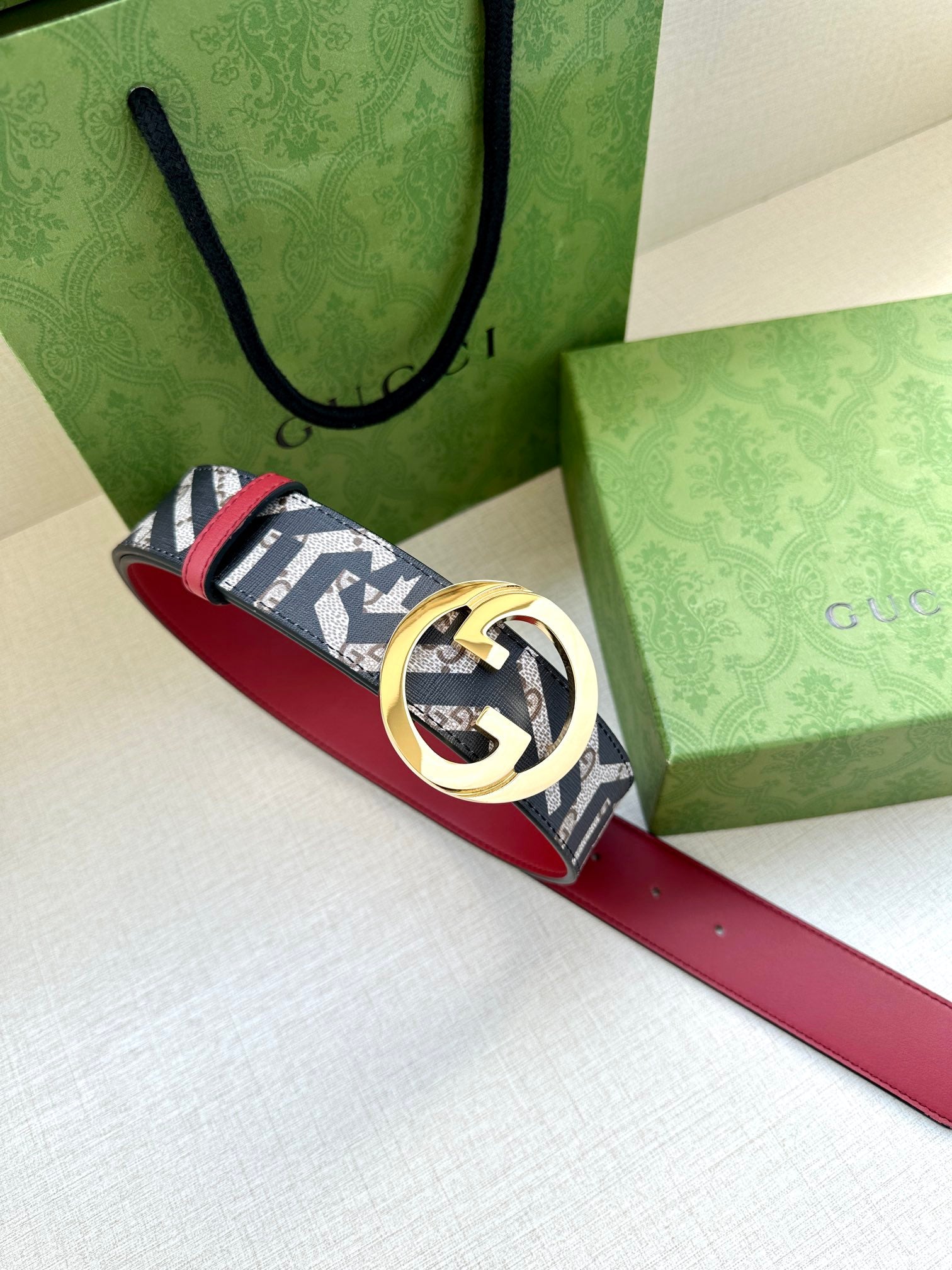 Gucci belt lying across boxes: red strap with navy-and-white logo canvas and gold buckle